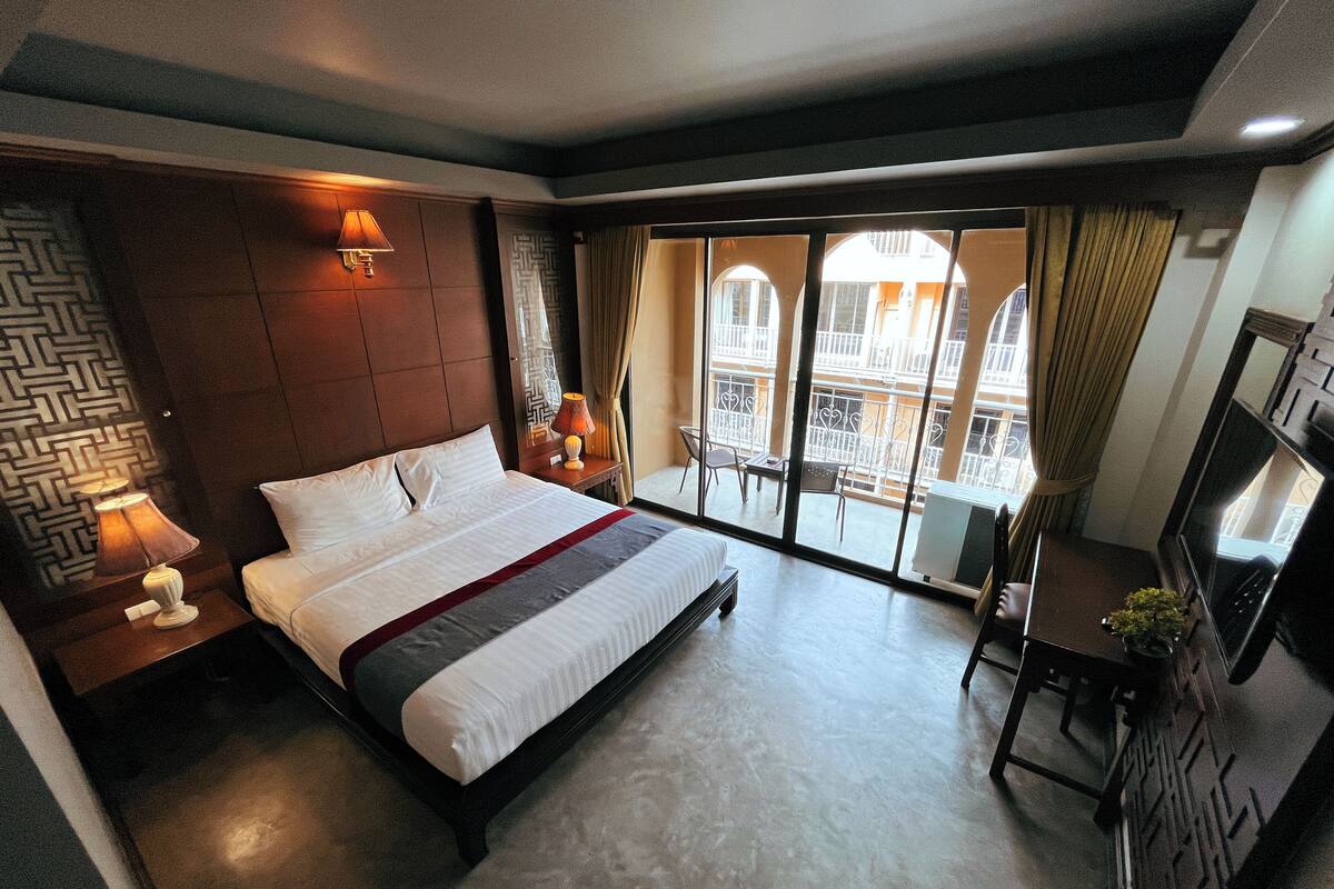 Ein Hotelzimmer mit einem großen Bett, einem Schreibtisch mit Stuhl, einem Fernseher und einem Balkon mit Blick auf die Stadt.