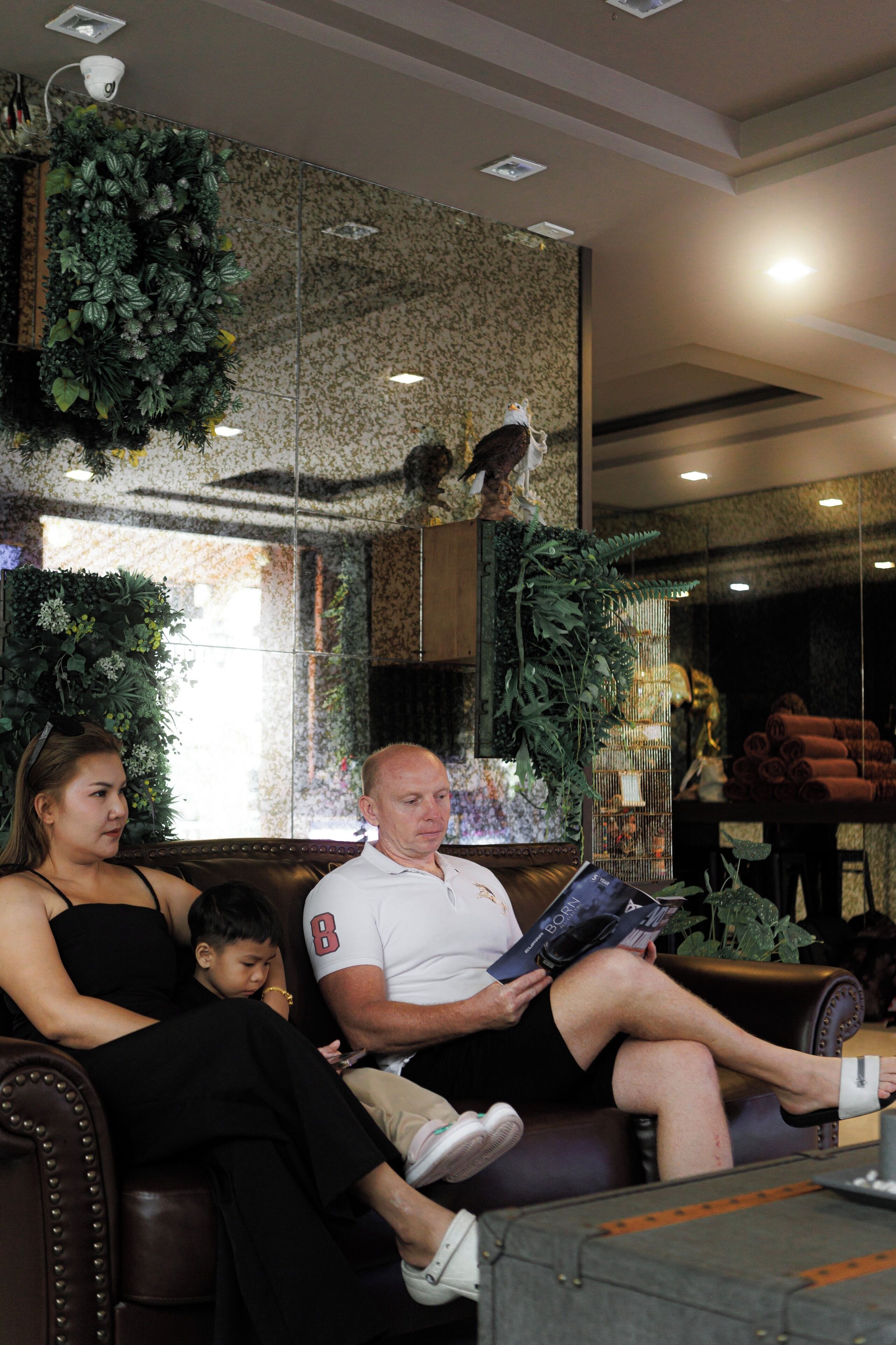 Eine Familie sitzt auf einer Ledersofa in einer Empfangshalle mit einer Wandgestaltung und einem großen Fenster.