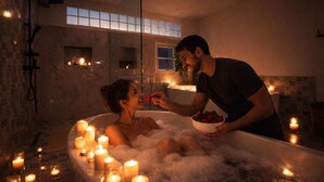 Una pareja en una bañera con velas, rodeada de burbujas.
