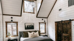 A bedroom with a large bed, a bench, a dresser, and a wardrobe. - Dreamcatcher Cottage- A Luxurious Romantic Escape in Hochatown (Broken Bow)
