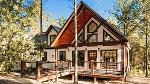 A cabin with a wooden deck, large windows, and a sloped roof. - Dreamcatcher Cottage- A Luxurious Romantic Escape in Hochatown (Broken Bow)