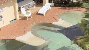 Une piscine au design incurvé, entourée d’une terrasse en briques et de chaises longues blanches.