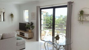 Un salon moderne avec un canapé, un téléviseur et une table en verre entourée de chaises.