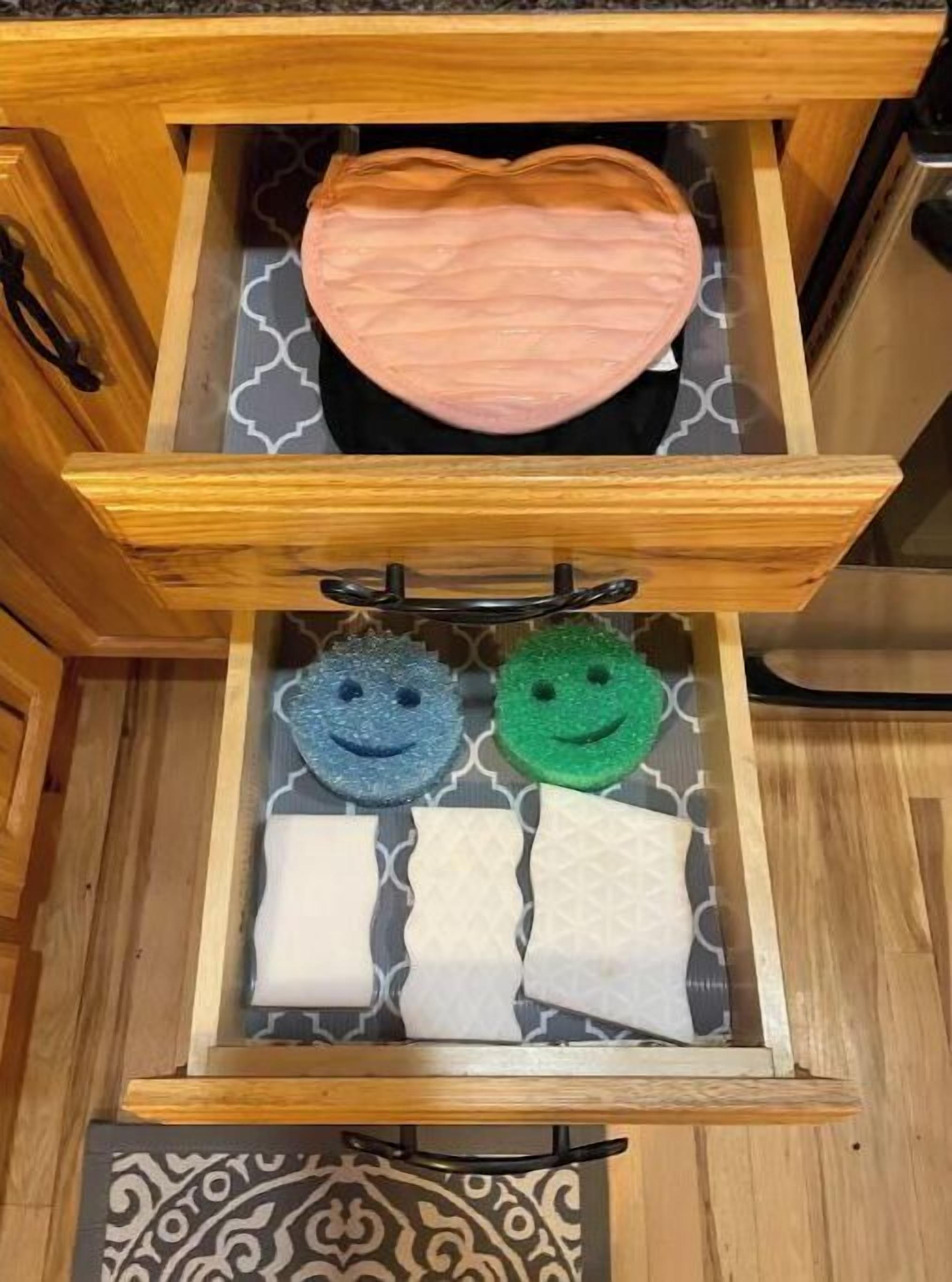 A wooden drawer with a patterned interior, containing a pink item and two sponge-like objects with smiley faces.
