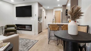 A modern living room with a fireplace, a dining area with a round table, and a kitchen in the background. - Resort-Style Brian Head Condo Near Slopes! (Brian Head)