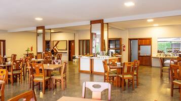 Un comedor amplio con varias mesas y sillas de madera, una estación central de servicio y vistas al exterior a través de amplios ventanales.