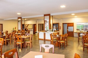 Un comedor amplio con varias mesas y sillas de madera, una estación central de servicio y vistas al exterior a través de amplios ventanales.