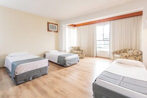 A hotel room with two single beds, a sofa, a chair, a window with curtains, and a wall-mounted air conditioner. - Blumenau Tower (Blumenau)