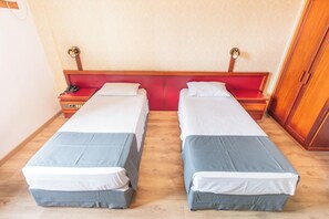Quarto com duas camas de solteiro, cada uma com cabeceira vermelha e roupa de cama branca. Tem uma mesa de cabeceira de madeira com um telefone em cima.