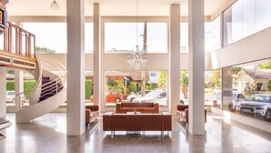 Eine geräumige Lobby mit einer zentralen Sitzgruppe, einer Wendeltreppe und großen Fenstern mit Blick auf die Straße.