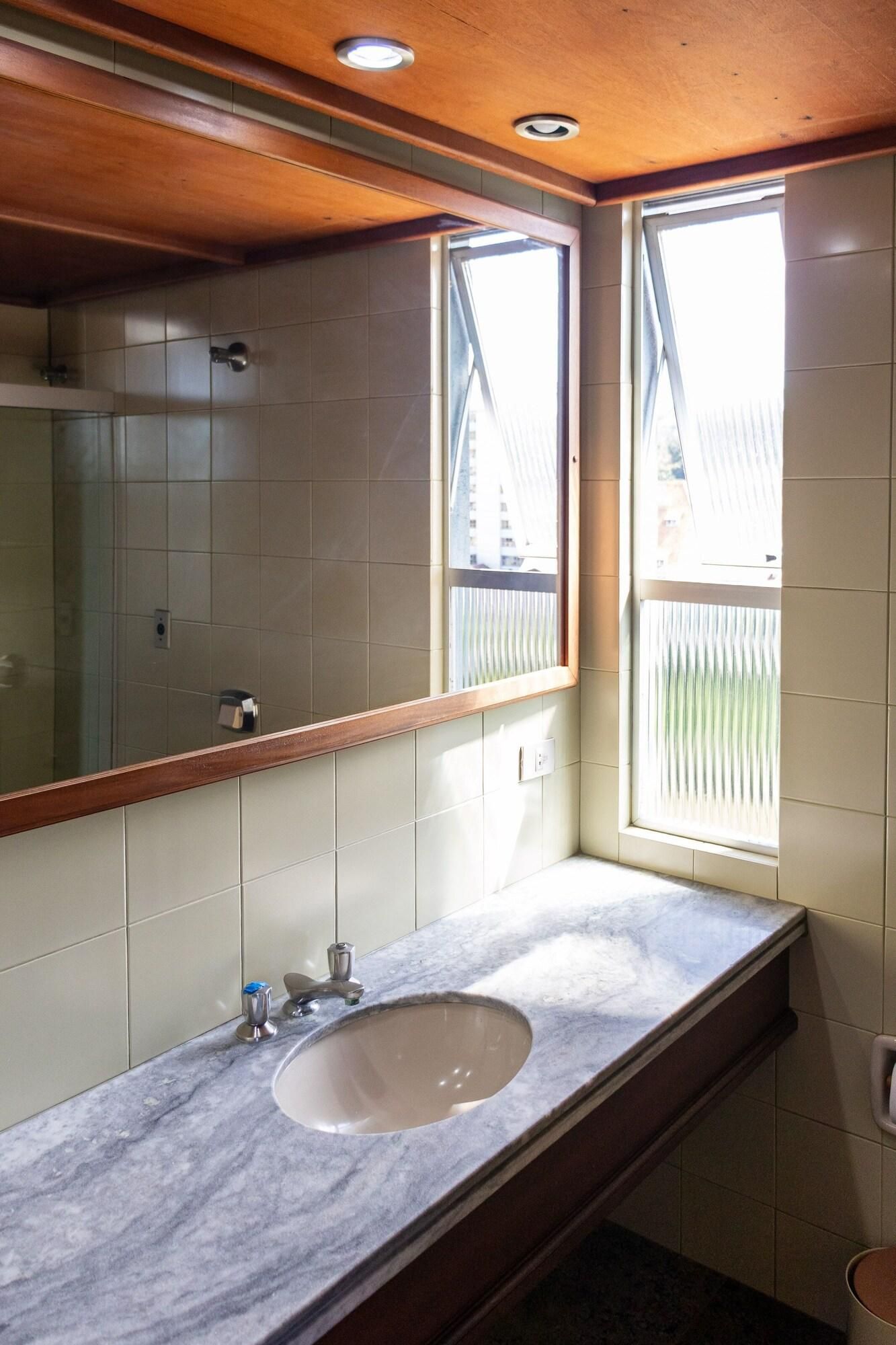 Un baño con lavamanos de mármol, un espejo grande y una ventana con persianas.