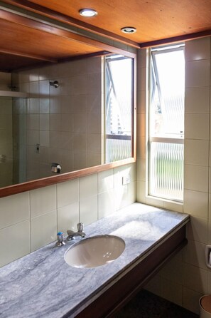 Ein Badezimmer mit Marmorwaschbecken, einem großen Spiegel und einem Fenster mit Jalousien.