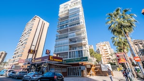 Un edificio de varios pisos con bar y restaurante en la planta baja, rodeado de coches aparcados y palmeras.