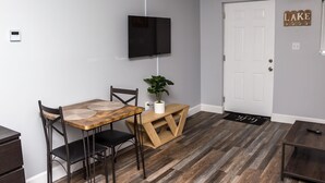 A dining area with a wooden table, two chairs, a potted plant, and a TV mounted on the wall.