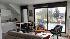 A modern living space with a sofa, dining table, chairs, and a kitchen area. - Guidel. Superb apartment with large terrace. (Guidel)