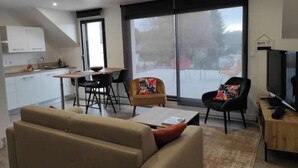 A modern living room with a sofa, a coffee table, and a TV. There is a dining area with a table and chairs, and a kitchen in the background. - Guidel. Superb apartment with large terrace. (Guidel)