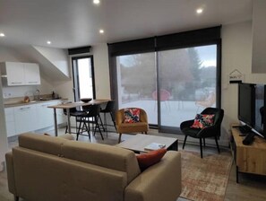 A modern living room with a sofa, a coffee table, and a TV. There is a dining area with a table and chairs, and a kitchen in the background. - Guidel. Superb apartment with large terrace. (Guidel)