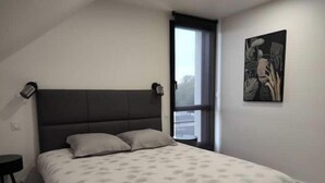 A bedroom with a bed, a nightstand, a window, and a painting on the wall. - Guidel. Superb apartment with large terrace. (Guidel)