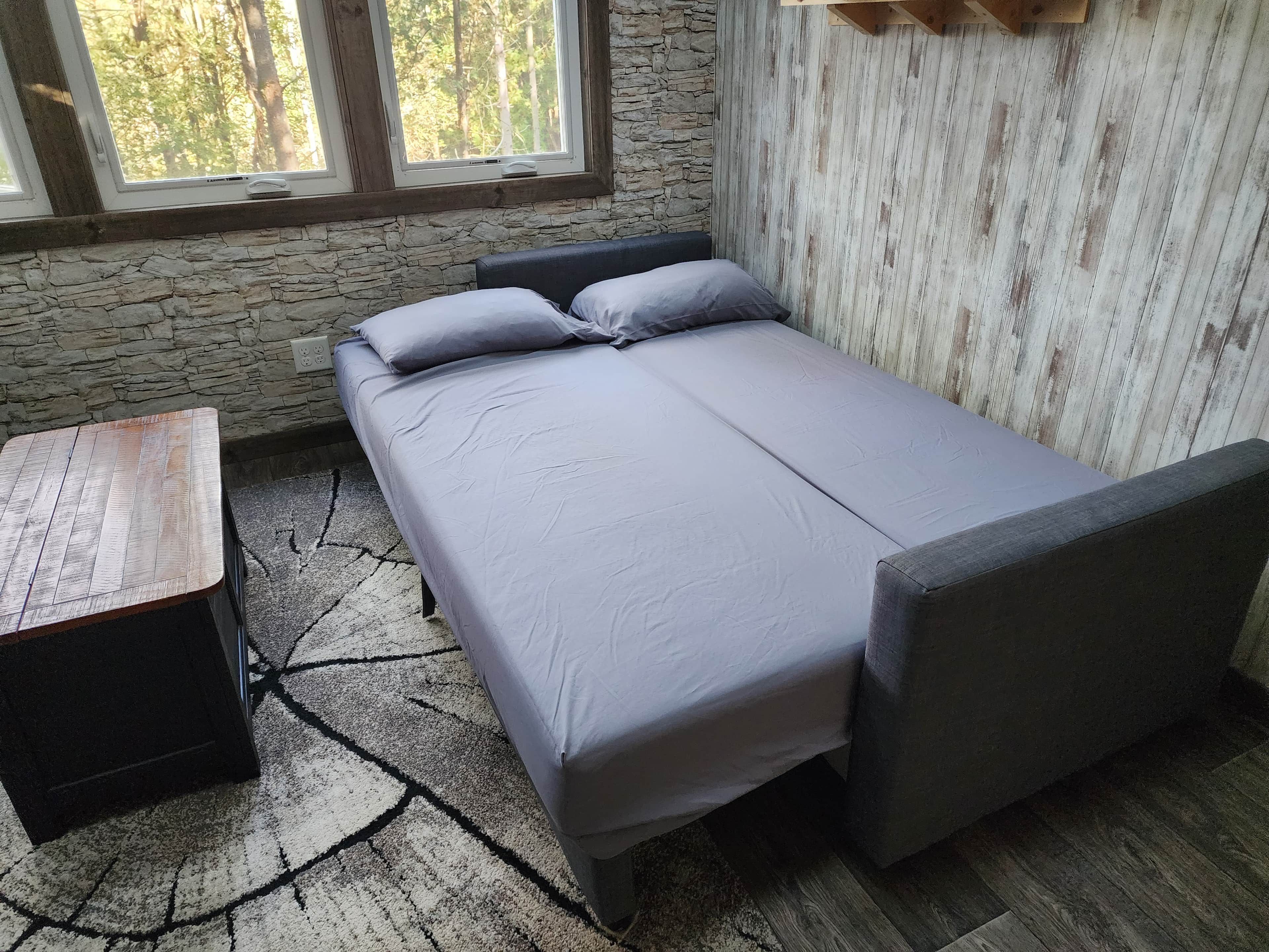 Ein Einzelbett mit Kopfteil, ein kleiner Tisch und eine Steinwand mit Fenster.