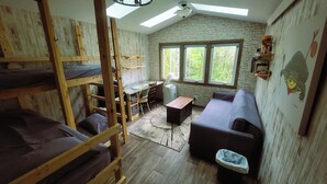 Una habitación rústica con literas, un sofá, una mesita y una ventana con vistas a árboles.