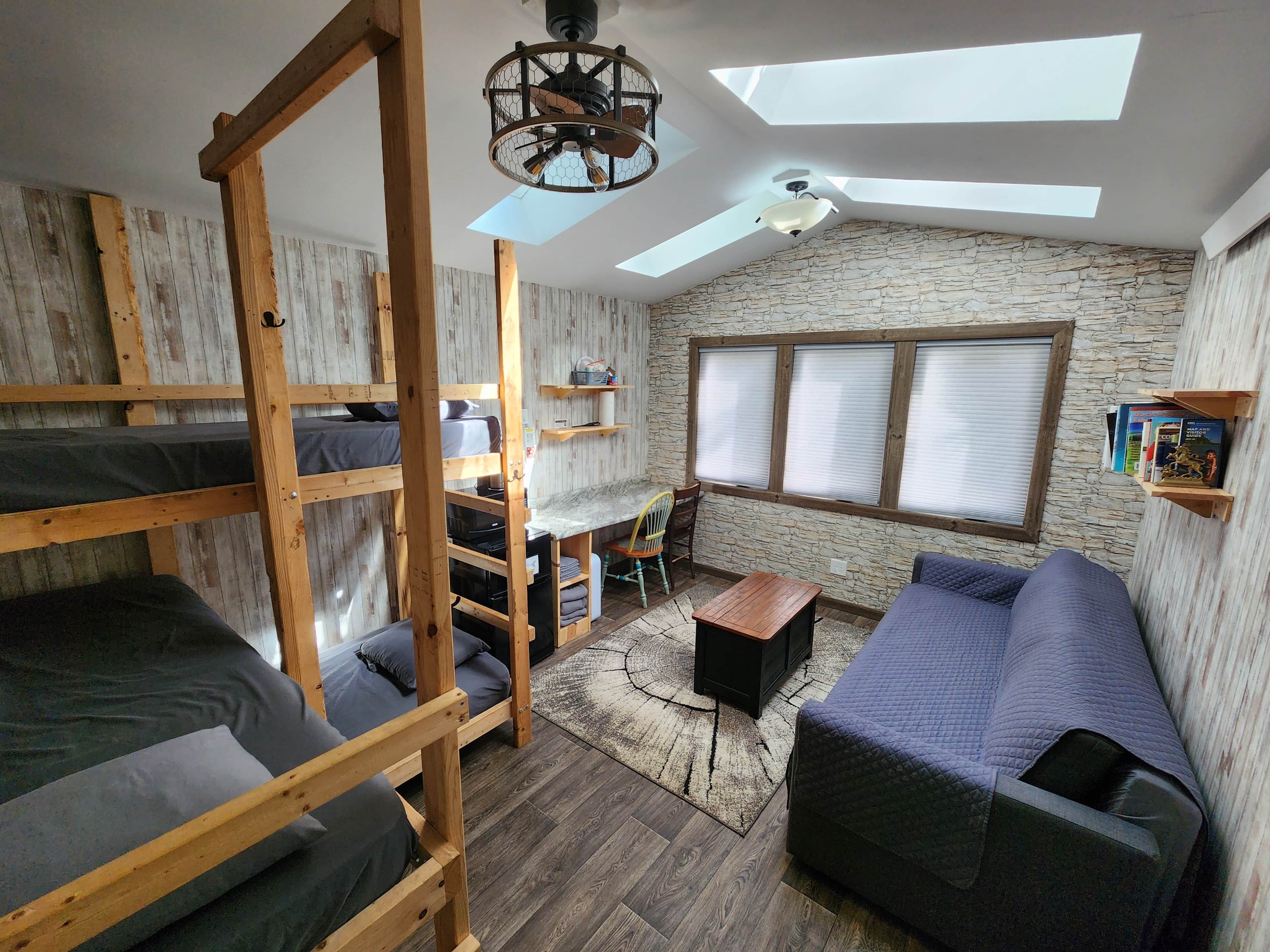 A room with bunk beds, a sofa, a desk, and a ceiling fan.