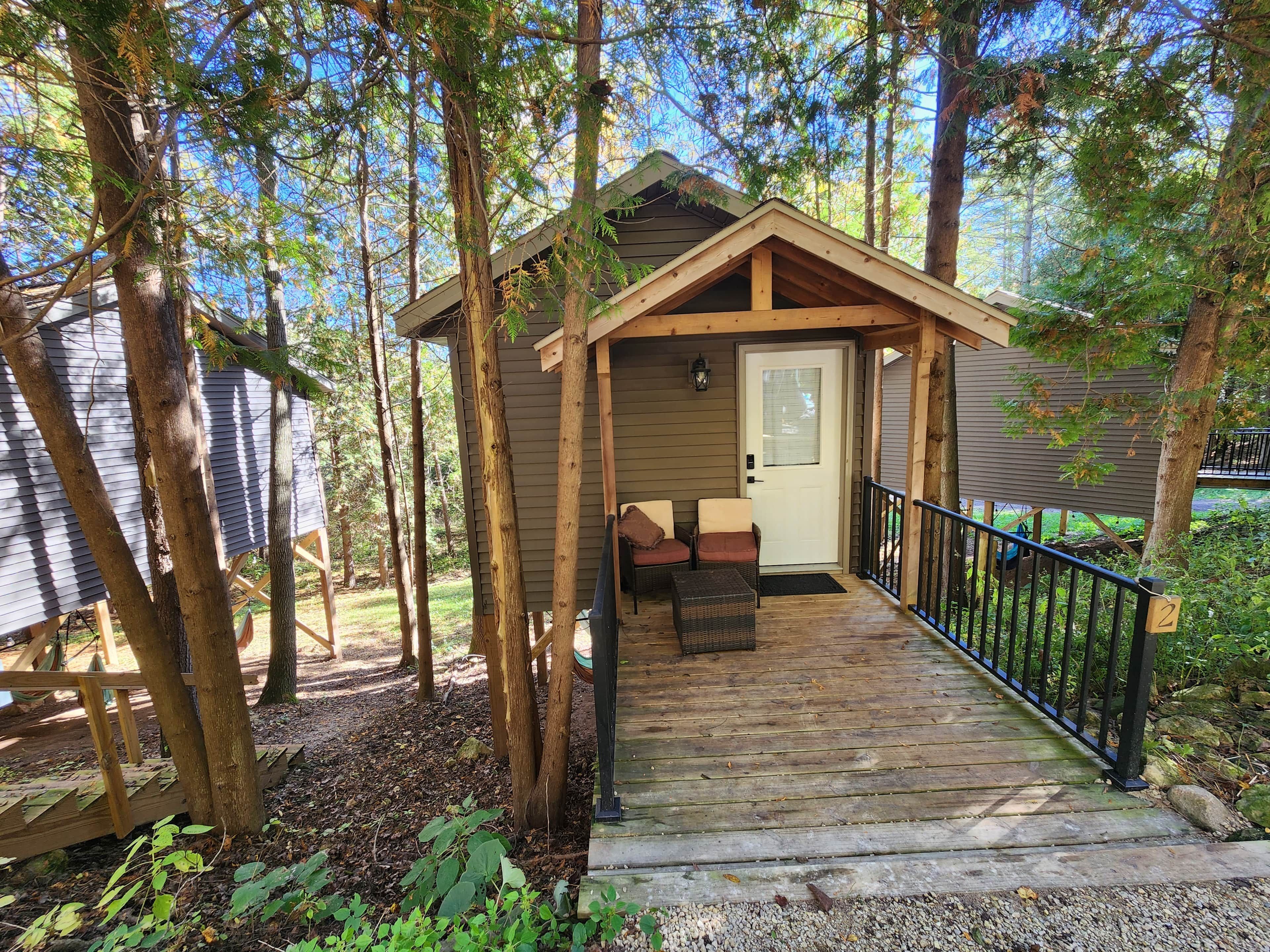 A wooden cabin with a porch, a door, and a small seating area with two chairs.