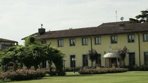 A yellow building with a tiled roof, a sign reading "La Muratella," and a well-maintained garden with flowers and shrubs.