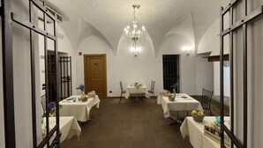 A dining area with tables set for four, a chandelier, and a wooden door.