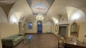 A spacious room with a high arched ceiling, a chandelier, a green sofa, a wooden table, and a fireplace.