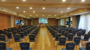 A conference room with rows of chairs, a podium, and a projection screen at the front.