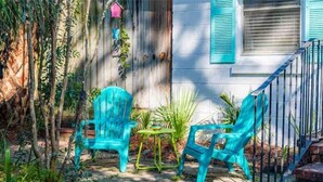 A patio with two turquoise chairs and a small table, surrounded by greenery and a wooden fence.