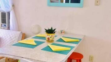A small dining area with a table, colorful stools, a potted plant, and a window with a blue frame.