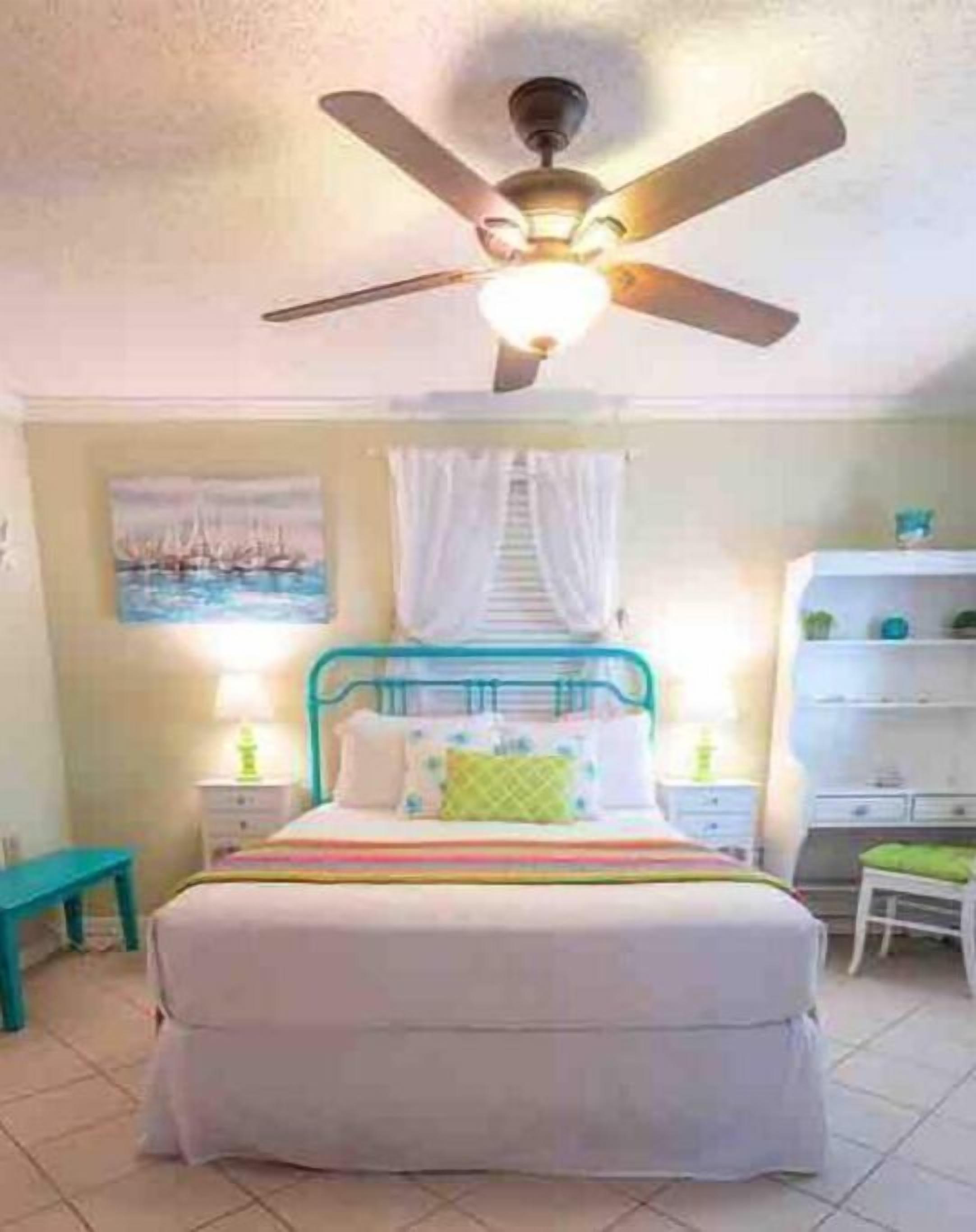 A bedroom with a bed, a ceiling fan, a nightstand, a chair, and a shelf with decorative items.