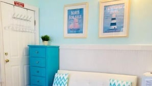 Habitació amb un sofà blanc, una petita còmoda turquesa i una alfàbrega amb dibuixos.