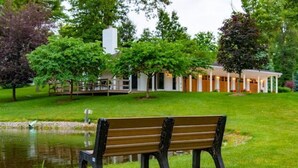 Un banc dans un parc, près d’un étang, entouré d’arbres et d’un bâtiment doté d’un porche abrité.