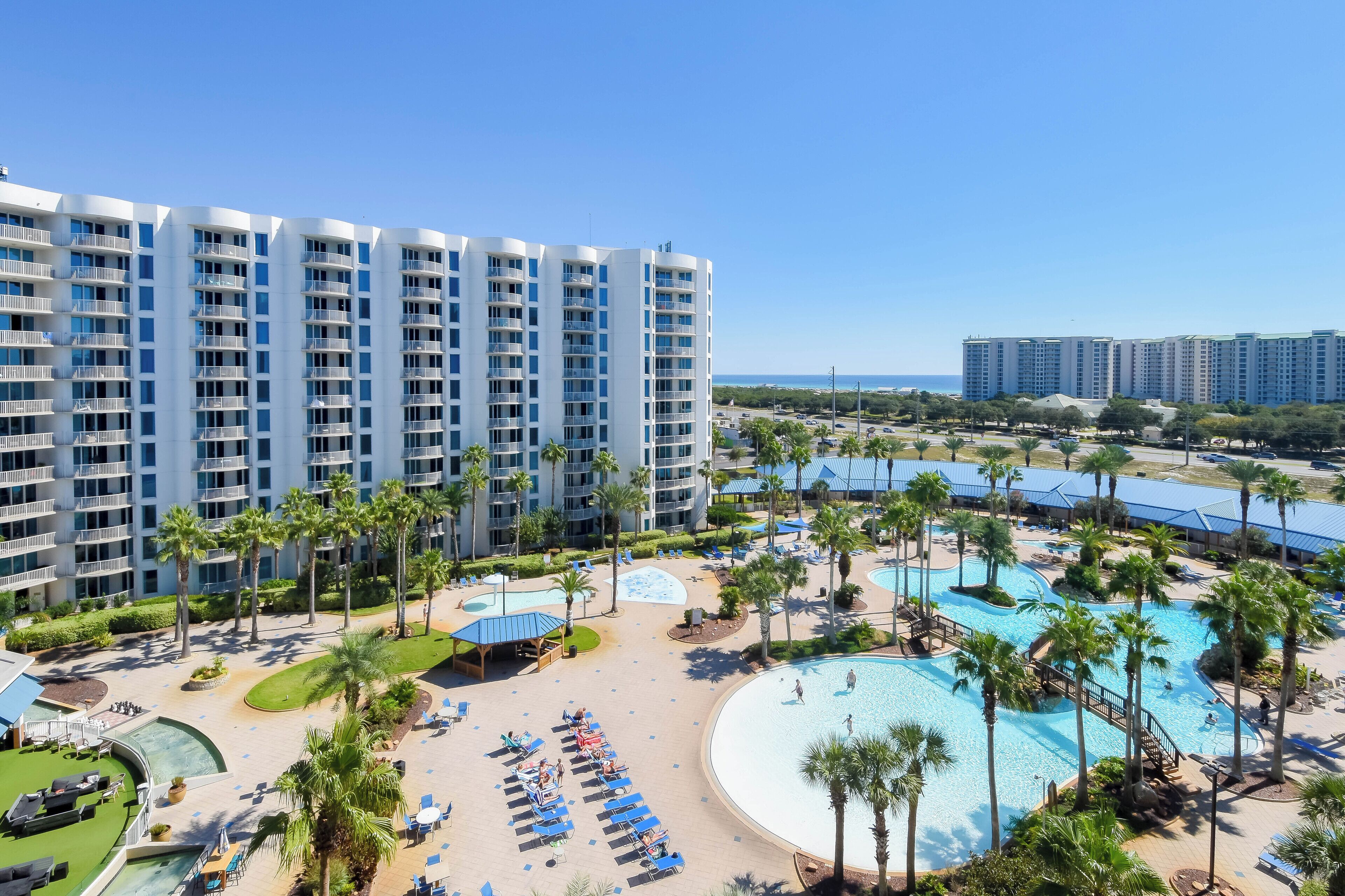 A high-rise hotel with multiple balconies, a swimming pool area with sun loungers, and palm trees.