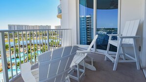 Un balcón con sillas Adirondack blancas, una puerta de cristal y vistas a una piscina y edificios.