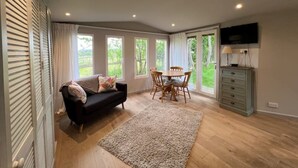 A spacious room with a black sofa, a wooden dining table with chairs, a grey dresser, and a television mounted on the wall.
