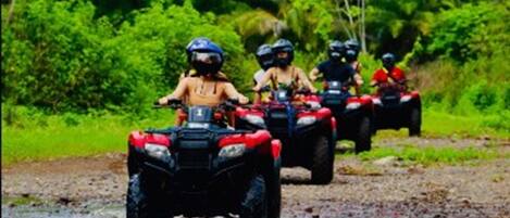A group of people riding ATVs on a muddy path surrounded by lush greenery.