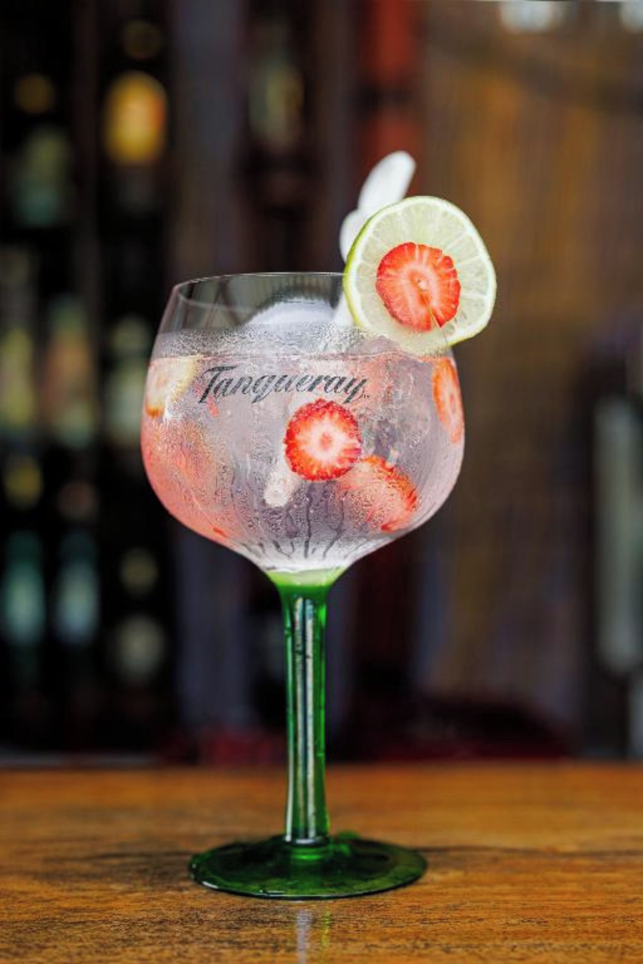 A cocktail glass with a lime slice and a strawberry garnish on a bar counter.