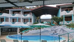 A pool area with lounge chairs and umbrellas, a bar, and a building with multiple balconies. - Hotel Planeta Sano (Quepos)