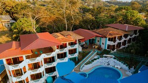 A multi-story hotel with balconies, a swimming pool, and a surrounding garden. - Hotel Planeta Sano (Quepos)