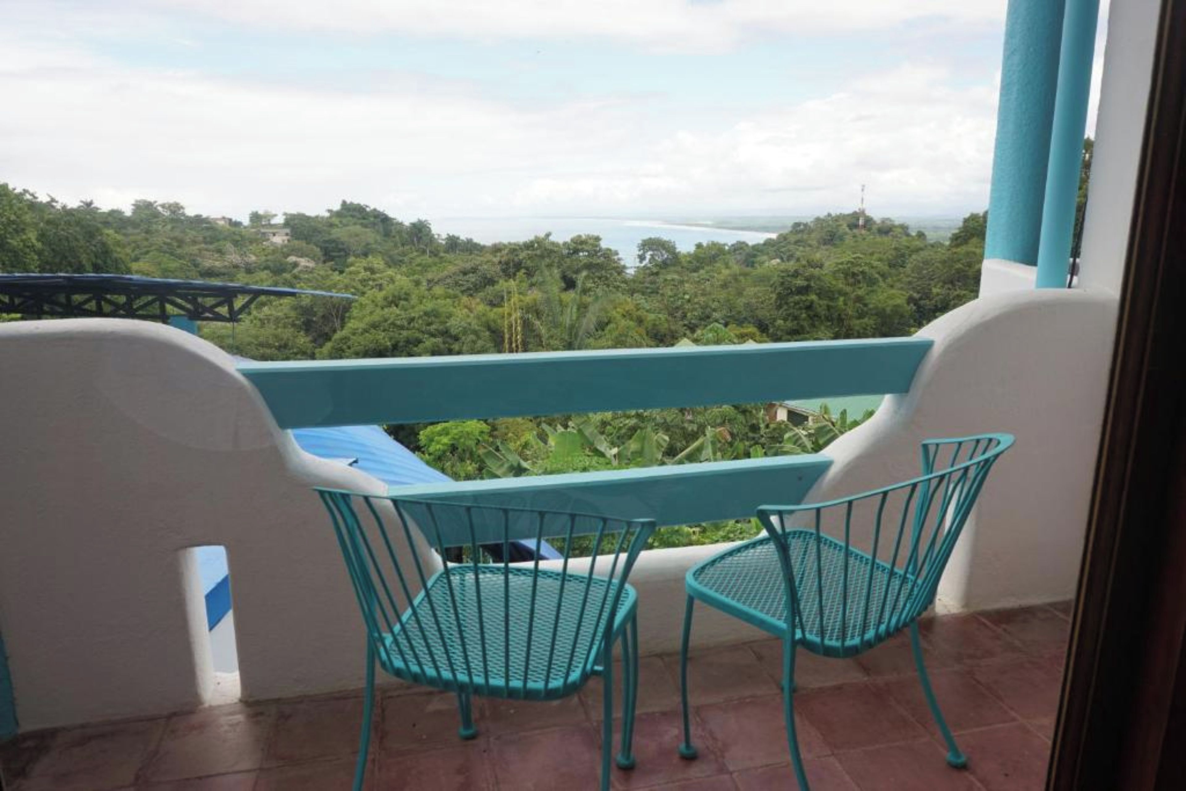 A balcony with two chairs and a table, overlooking a lush landscape with trees and a body of water.