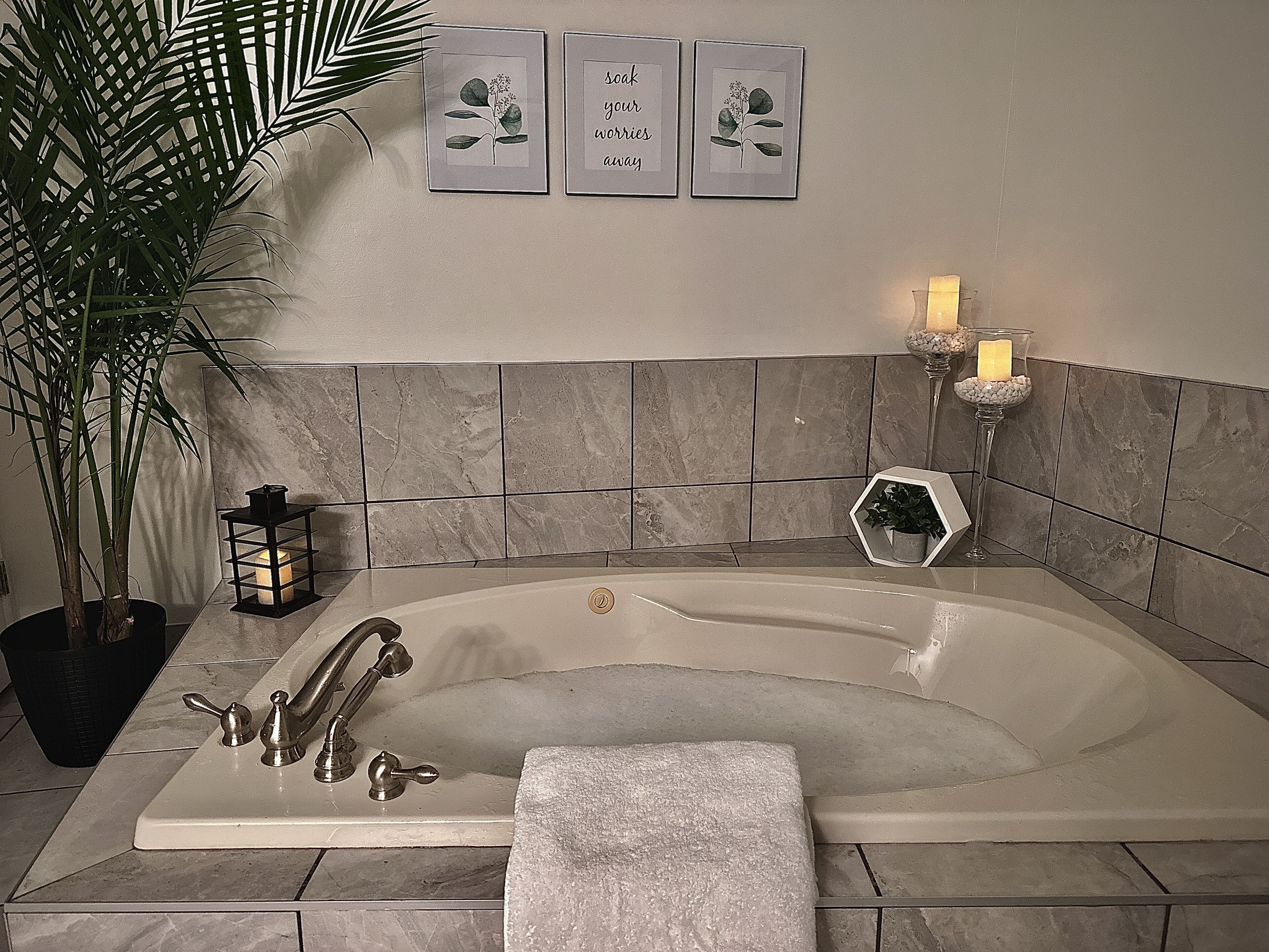 A bathroom with a freestanding bathtub, a potted plant, a candle, and framed botanical prints on the wall.
