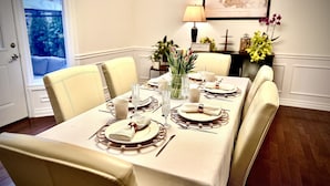 A dining table set for six with a white tablecloth, gold-rimmed plates, and a vase of tulips.