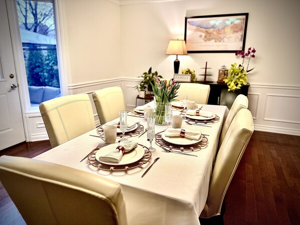 A dining table set for six with a white tablecloth, gold-rimmed plates, and a vase of tulips. - Settlers Suites (Niagara-on-the-Lake)