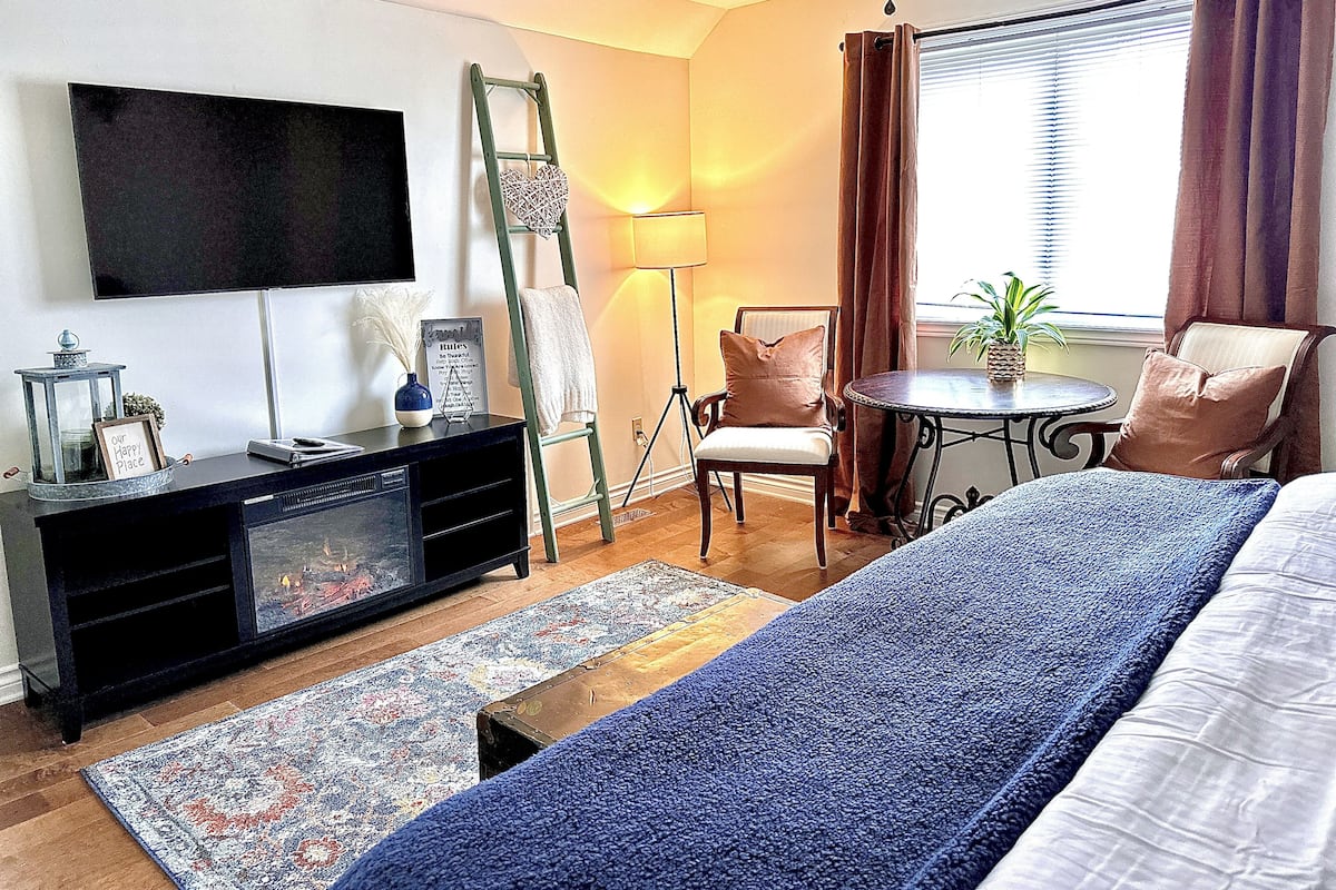 Habitación de hotel con cama, televisión, escritorio, silla, mesita con planta y ventana con cortinas.