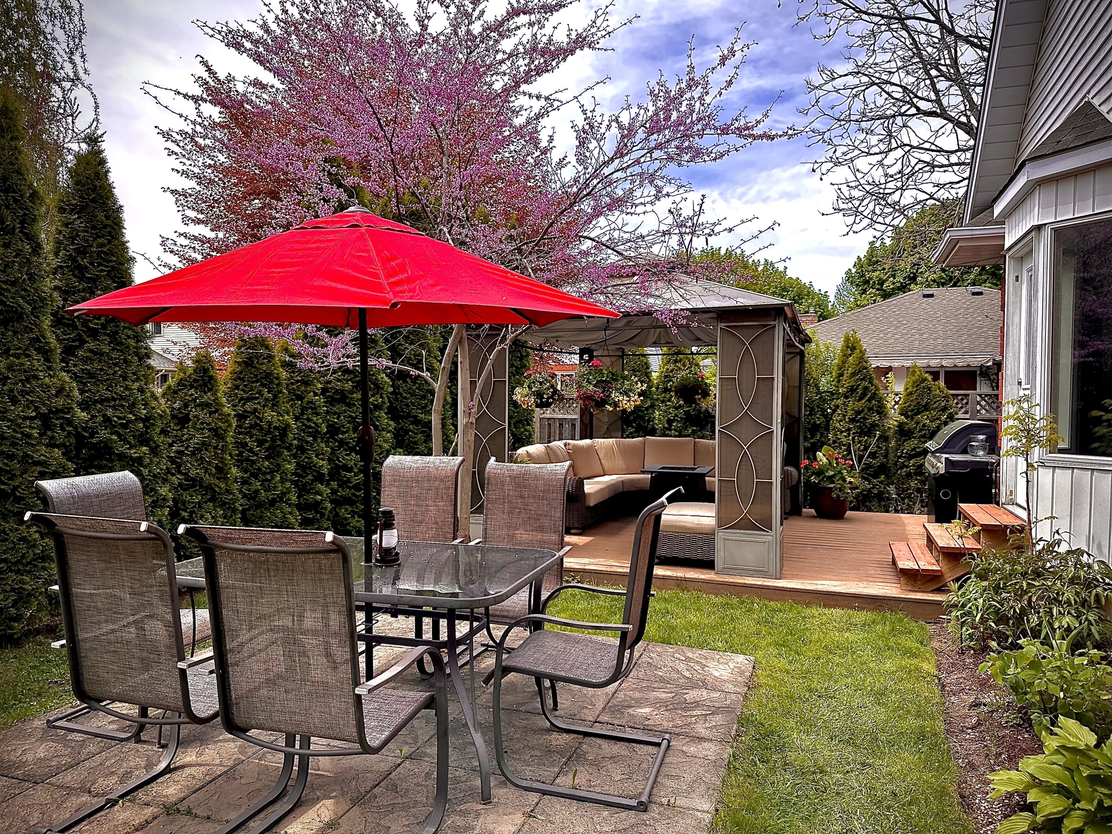 Une terrasse extérieure avec une table et des chaises, un parasol rouge et un espace salon abrité.