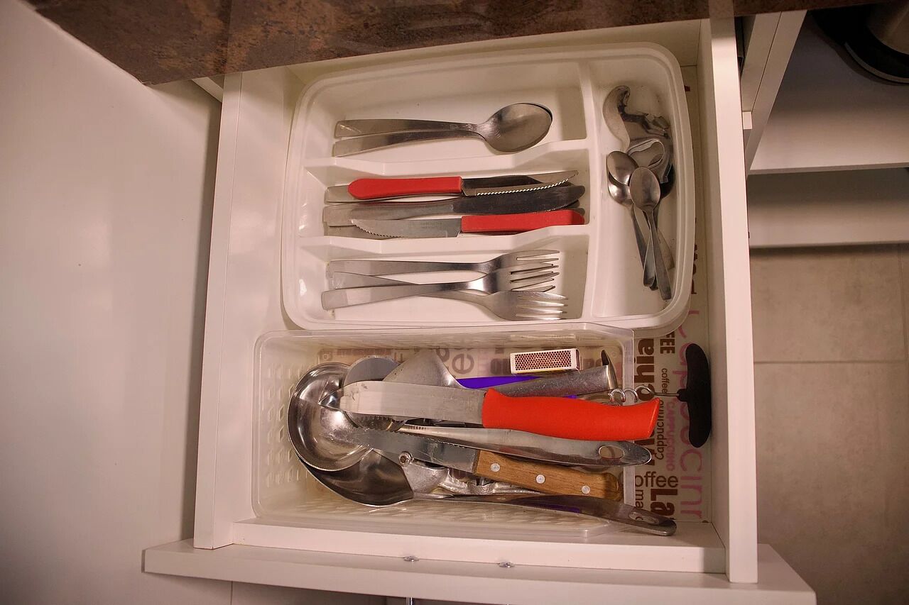 A drawer containing various kitchen utensils, including spoons, forks, and a large cleaver.