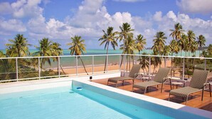 Une piscine sur le toit, dotée de chaises longues et offrant une vue sur la plage et les palmiers.